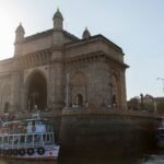 Stunning view of the iconic Gateway of India with boats and visitors at sunset in Mumbai.