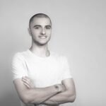 Grayscale portrait of a confident young man with crossed arms and a subtle smile.