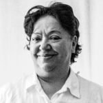 Black and white portrait of a smiling woman in a white shirt indoors.