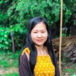 Outdoor portrait of a smiling woman in a yellow polka dot dress with lush greenery background.