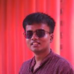 Portrait of a smiling man with sunglasses against a red backdrop, exuding style.