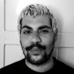 Expressive black and white portrait of a young man with light hair and beard indoors.
