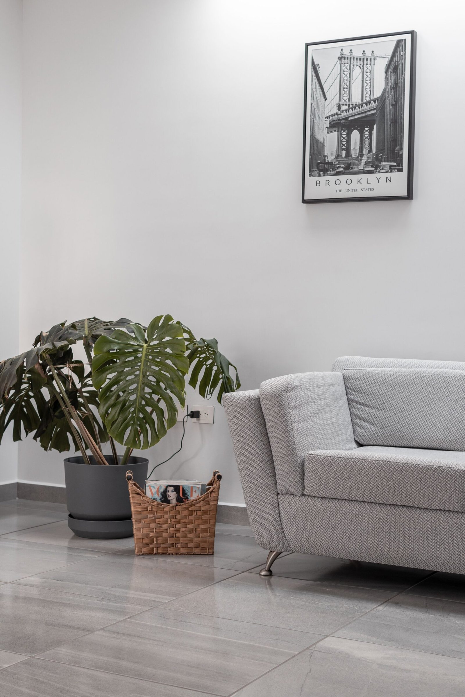 Minimalist living room featuring a couch, plant, and Brooklyn Bridge artwork.