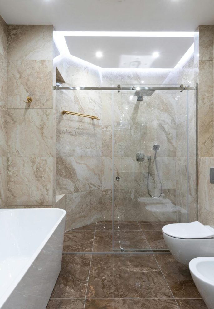 Interior of contemporary bathroom with marble walls and comfortable shower cabin under bright light of lamp